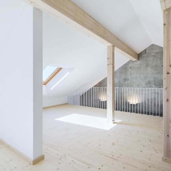 Dachgeschoss-Raum mit Blick auf Sicht-Holzbalken und Betonwand