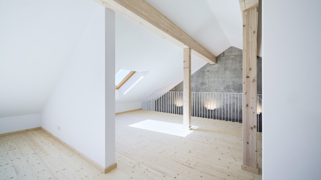 Dachgeschoss-Raum mit Blick auf Sicht-Holzbalken und Betonwand